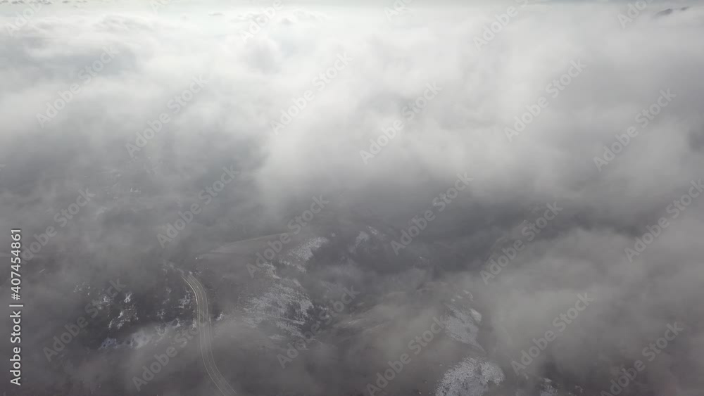 An aerial view of a snowy mountain pass while flying through hazy clouds An aerial view of a snowy mountain pass while flying through hazy clouds