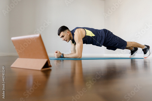 A young sports man does a plank exercise in self-isolation conditions. Online training at home with a social distance. Training all groups of mice by static load