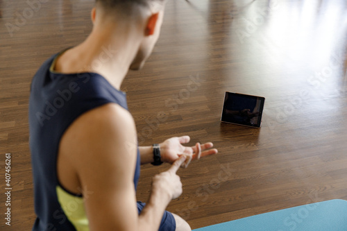 a young man trains in self-isolation during quarantine. The coach conducts an online training session. The guy looks at the tablet and shows the exercise. focus camera in device