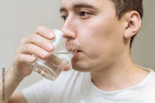 Young man drinks clean water from a transparent glass close up