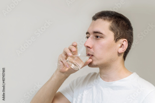 Young man drinks clean water from a transparent glass close up