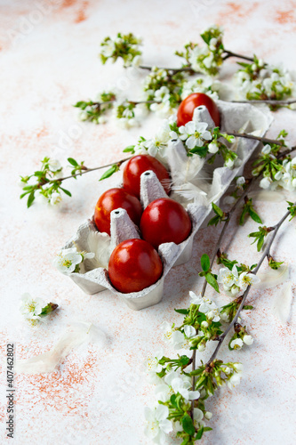 Red Easter eggs with spring flowered brunches on the light beige background. Vertical shot