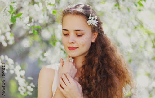 Portrait close up of cute young woman in a spring blooming garden on a white flowers background