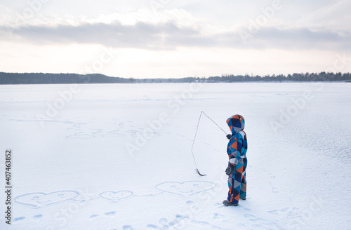 boy in a multi-colored winter overalls in an open snow-covered space, with a stick in the snow, draws hearts, enjoys the winter. Winter fun in nature. Love Winter
