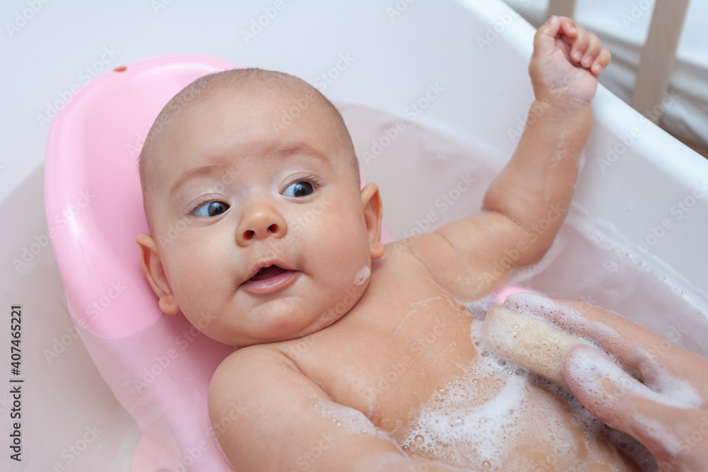 Mom's hand with a sponge washes the baby in the bathroom Mom's hand with a sponge washes the baby in the bathroom