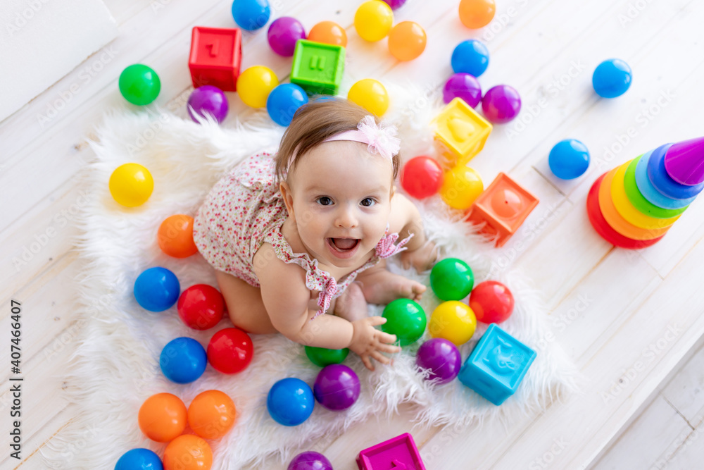 Obraz premium happy little girl sitting in a white room in a red dress with bright toys and looking at the top