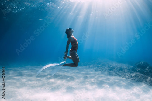 Woman freediver in red swimsuit with white fins posing underwater in tropical ocean. Sporty girl dive underwater.