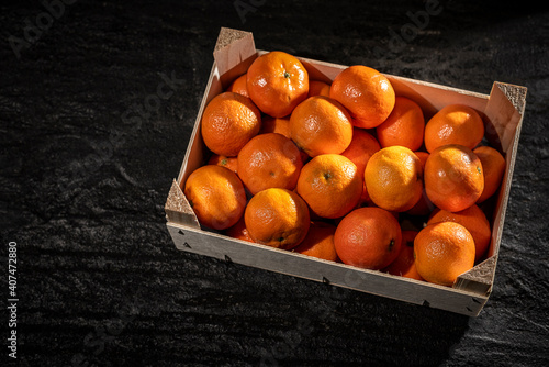 Tangerines (oranges, clementines, citrus) in wooden box on garnet tiles background. Top view.Tangerines (oranges, clementines, citrus) in wooden box on black background. Top view.