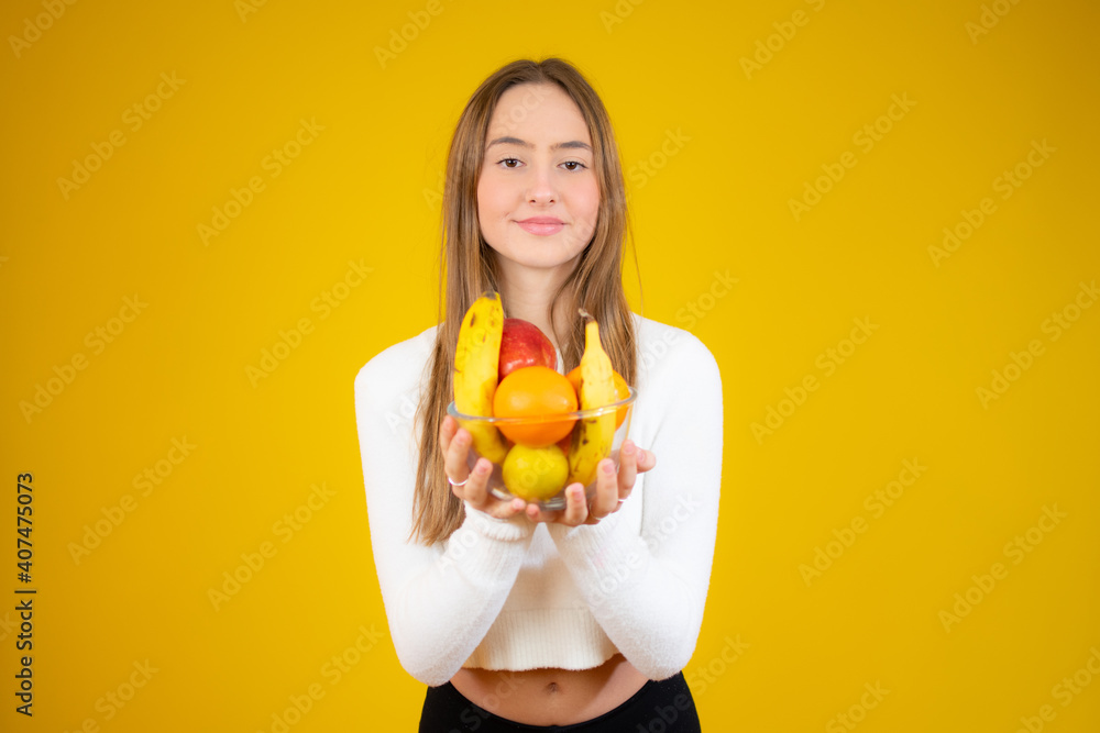 Happy beautiful girl holding bowl of fresh fruits, studio shot, isolated over yellow background Happy beautiful girl holding bowl of fresh fruits, studio shot, isolated over yellow background
