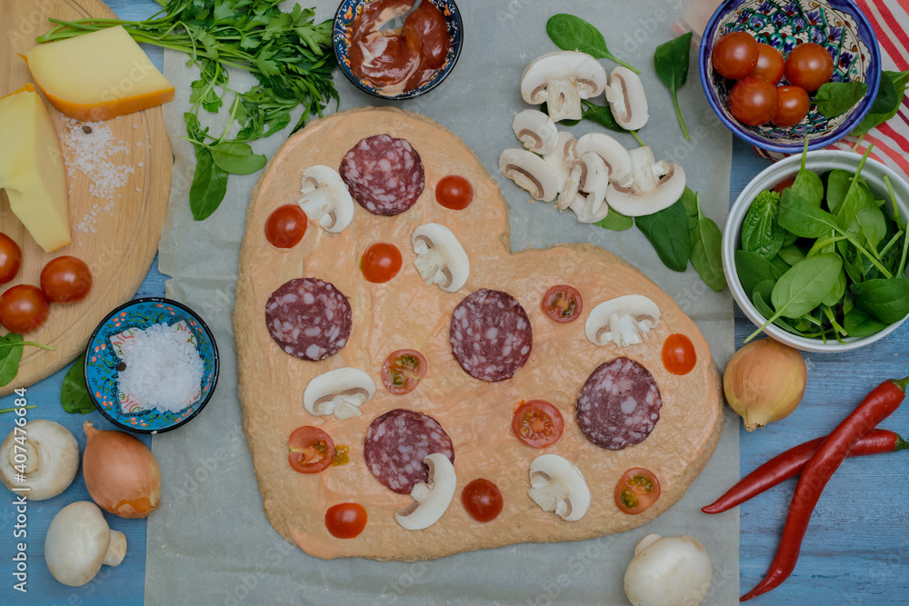 Homemade pizza for Valentine's Day.Delicious pizza heart made of yeast-free dough with healthy vegetables, tomatoes, herbs and cheese, prepared at home for a festive dinner