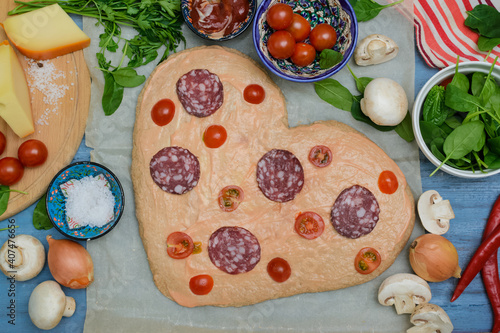 Homemade pizza for Valentine's Day.Delicious pizza heart made of yeast-free dough with healthy vegetables, tomatoes, herbs and cheese, prepared at home for a festive dinner
