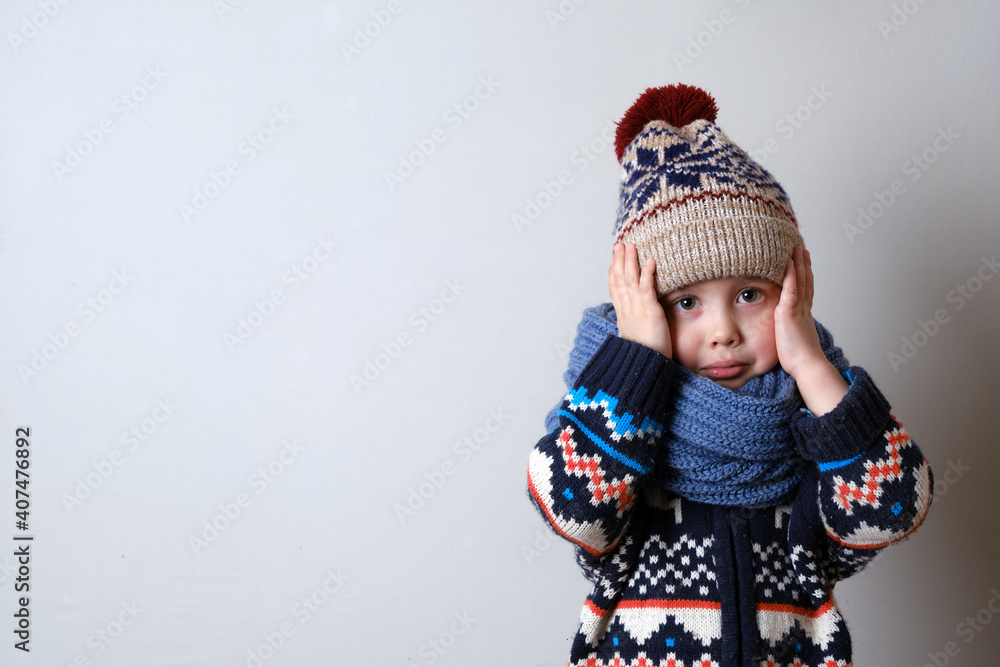 Sick child in clothes, toddler boy is standing on the grey background with a fever. llness child. Boy touches his head Sick child in clothes, toddler boy is standing on the grey background with a fever. llness child. Boy touches his head