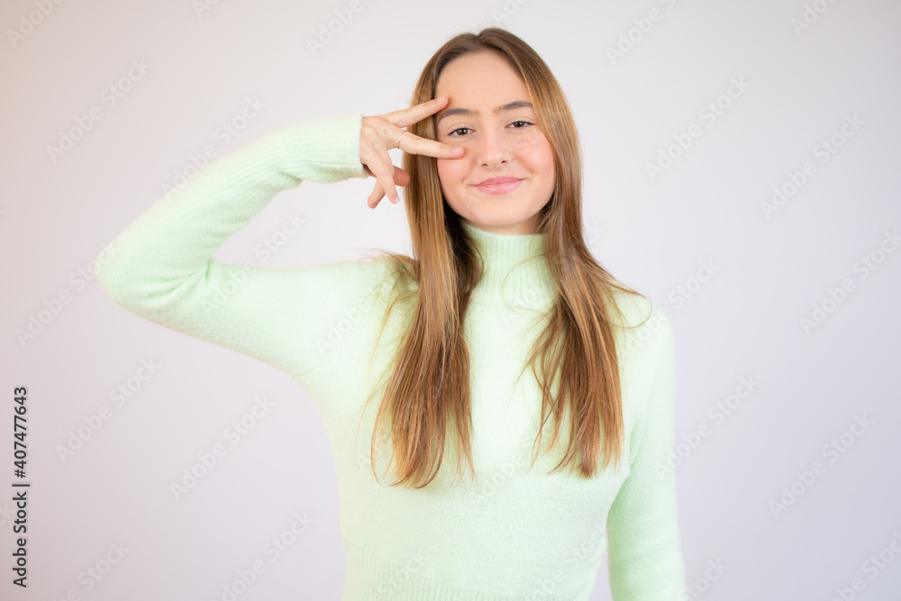 Attractive young girl, showing two fingers forming the letter V like victory, covering her eye with piece gesture Attractive young girl, showing two fingers forming the letter V like victory, covering her eye with piece gesture