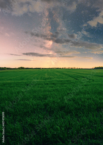 Green field at night with milky way and clouds 