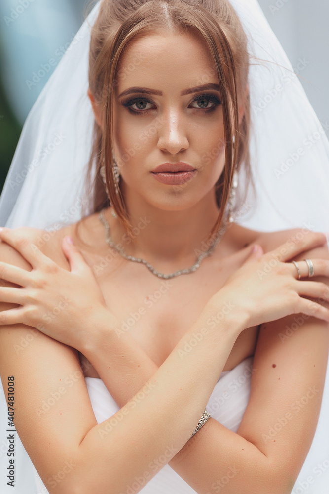 Fototapeta premium Beautiful bride in a magnificent wedding dress posing among greenery on the street. Bride concept for advertising dresses