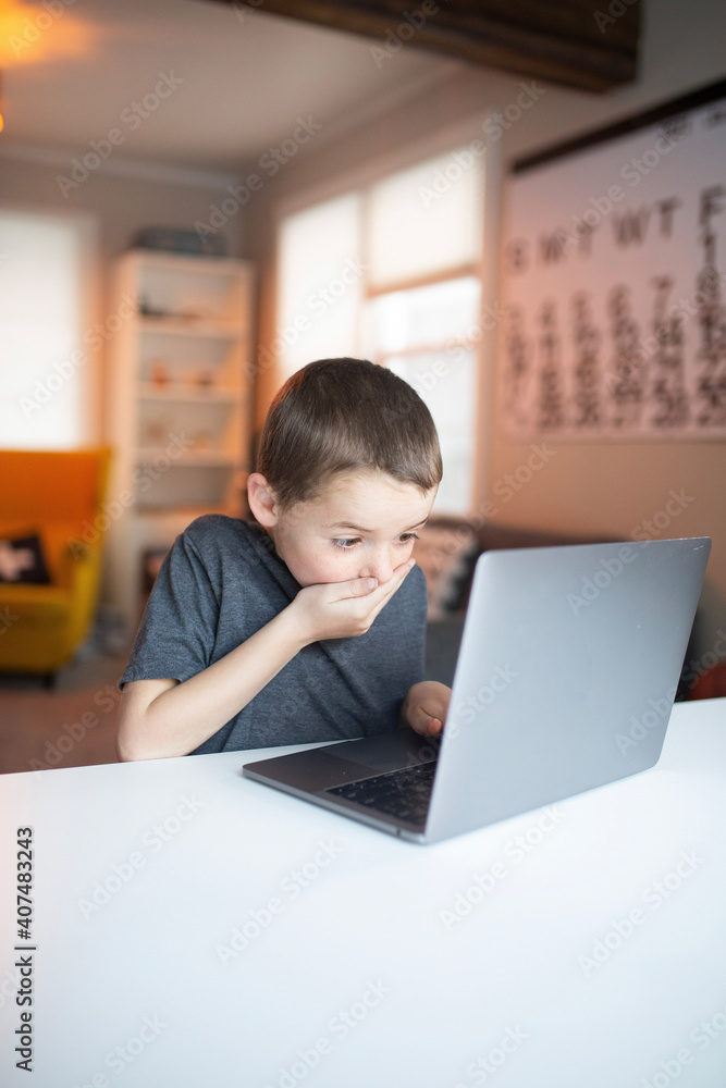 boy covering his mouth while looking at a laptop
