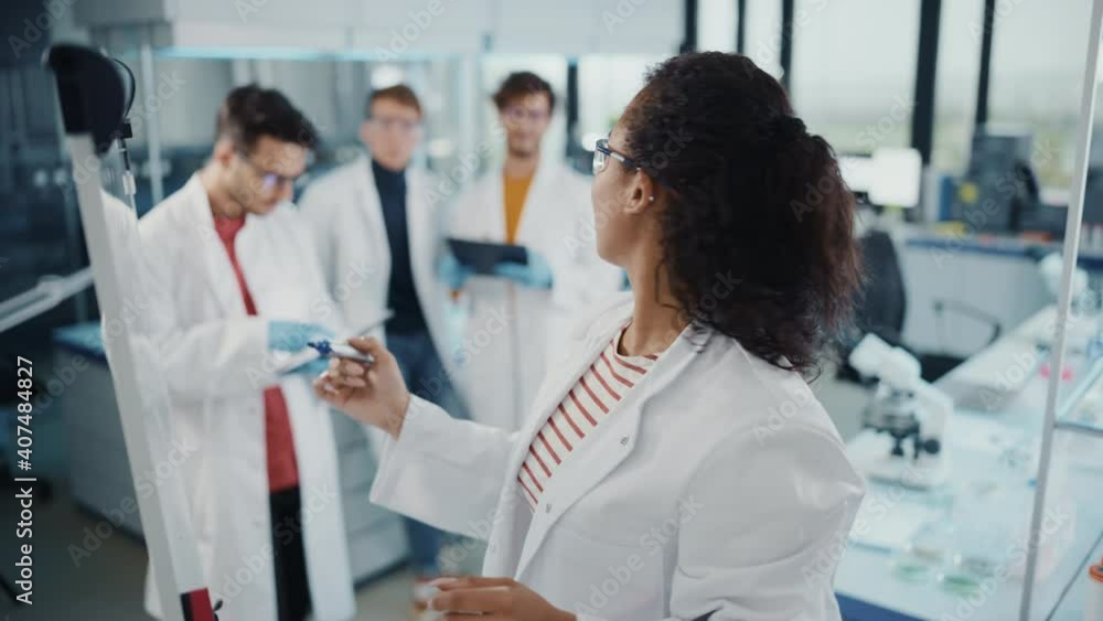 Medical Science Laboratory: Beautiful Black Female Scientist Writes Detailed Project Data Analysis on the Board, Her Diverse Team of Colleague Listens. Young Scientists Solving Problems. Elevated Shot Medical Science Laboratory: Beautiful Black Female Scientist Writes Detailed Project Data Analysis on the Board, Her Diverse Team of Colleague Listens. Young Scientists Solving Problems. Elevated Shot