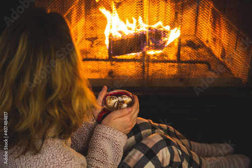 Young Caucasian girl in pyjamas sitting near the fire and holding a hot cup of chocolate. Concept about lifestyle and people.