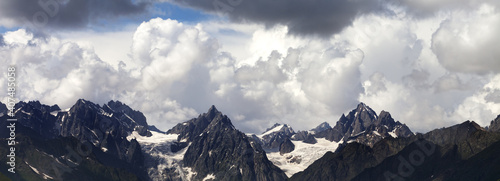 Panoramic view on high summer mountains with snow and glacier and cloudy sunlit sky