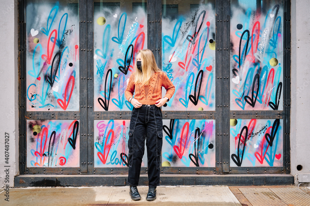 Girl wearing COVID 19 mask is posing full length by graffiti in