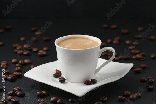 White cup of coffee on a black background. Coffee beans on a black table. Close-up side view  macro photography.