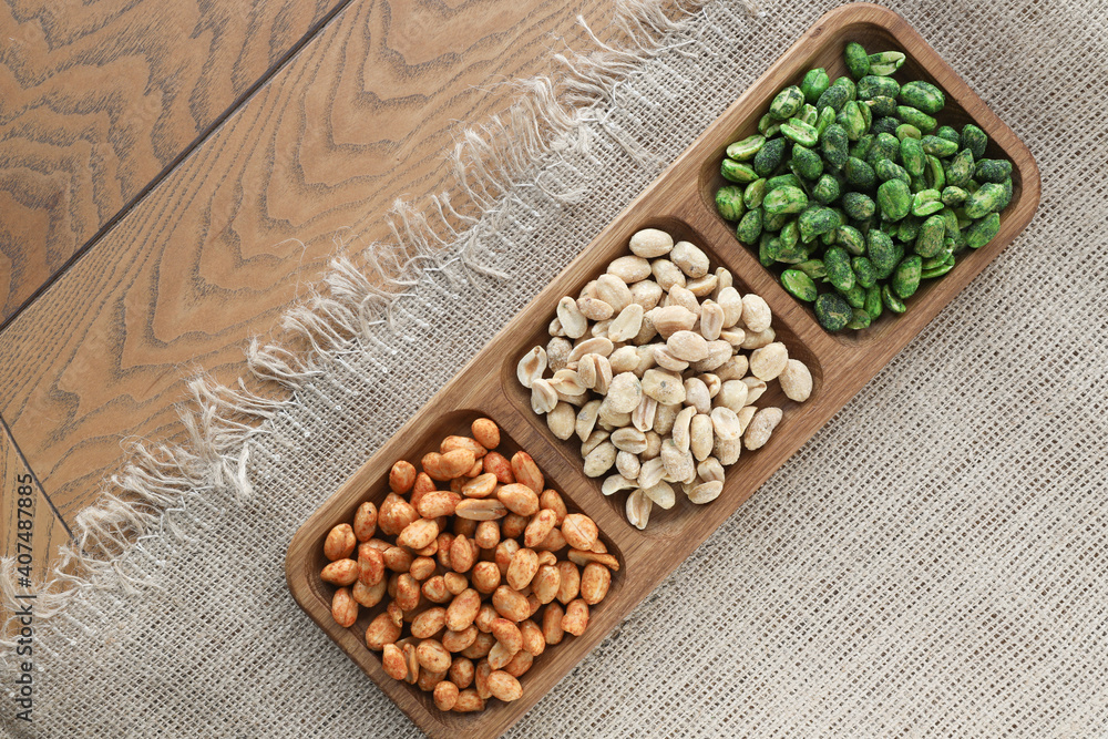 colorful roasted peanuts in a three-section wooden bowl that sits on a burlap tablecloth with colorful roasted peanuts in a three-section wooden bowl that sits on a burlap tablecloth with