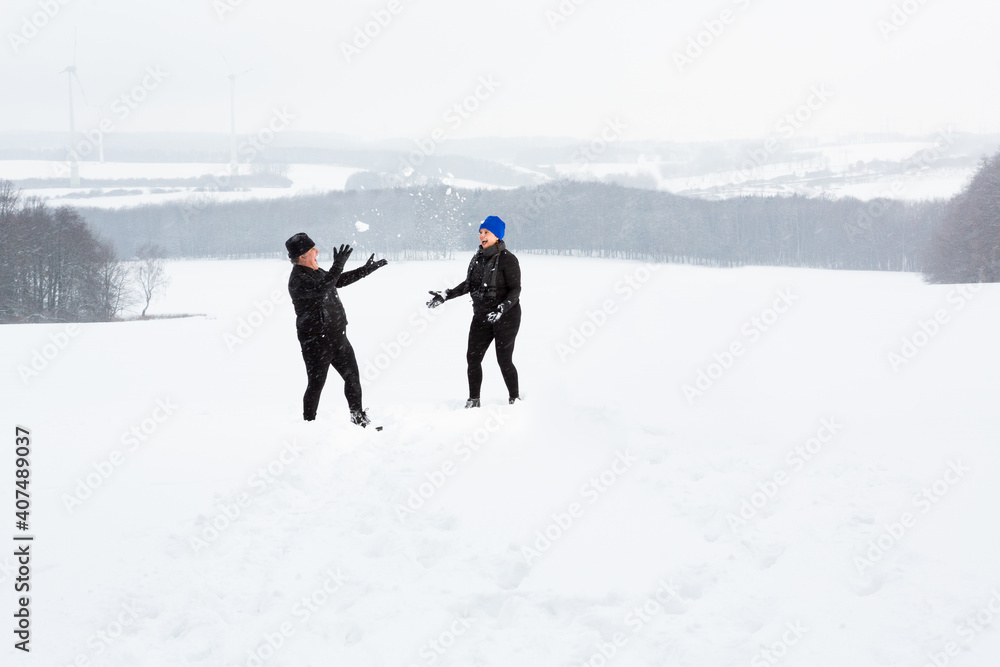 Couple plays in a open field with snow during a stormy winter day