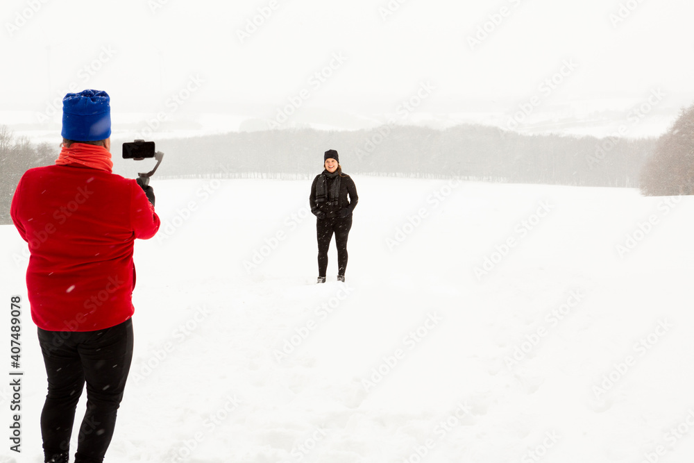 Man films his wife while she poses in the open field during a stormy winter day