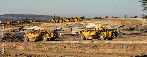 Earth moving equipment at a construction grading site with other tractors lined up in the background