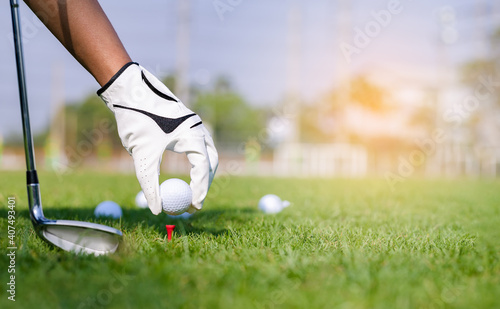 Hand in glove placing golf ball on tee in course. Golf helps to relieve tension and stimulate the brain function.