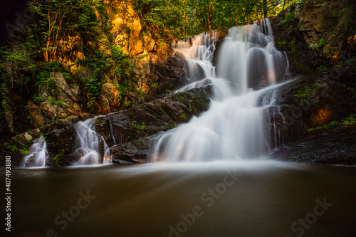 Long exposure of small waterfall in summer woods at sunset