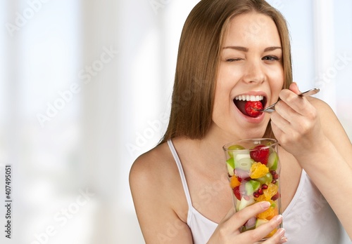 Young woman eating fruits from glass on blurred background