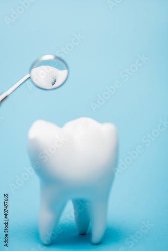 Close up view of dental mirror near model of tooth with crack on blurred foreground on blue background