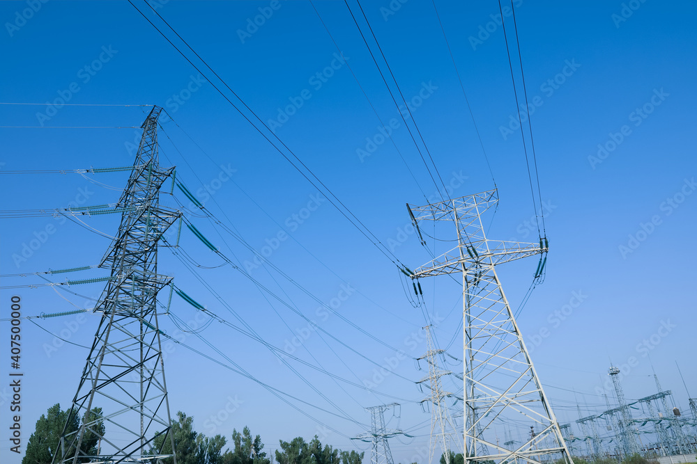 High voltage towers against blue sky on sunny day, low angle view