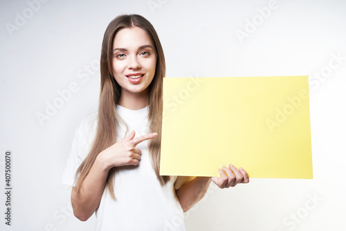 A beautiful blonde in a white T-shirt on a gray background holds a yellow sign