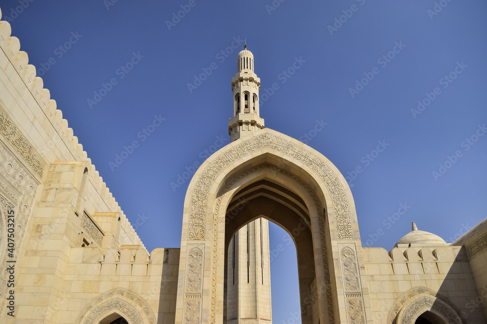 Arch, domes and minaret in Sultan Qaboos Grand Mosque in contrast with the blue sky. Oman.