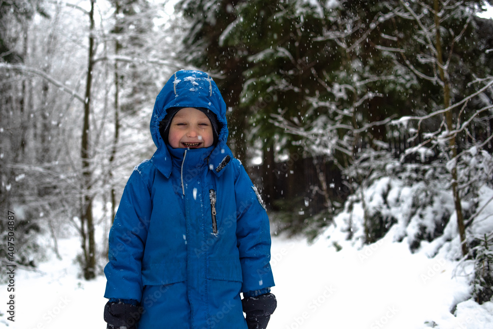 Happy boy laughs on the background of a winter snowy forest. It's snowing in the forest Happy boy laughs on the background of a winter snowy forest. It's snowing in the forest