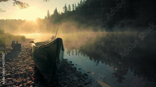 Locked down shot of river in New Brunswick, taken in early morning with sun shining down, and low mist hanging over, a boat is tied on shore. 