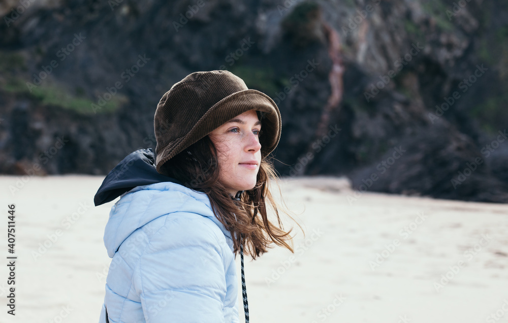 Soft light portrait of authentic young woman in her 20s sit at autumn or winter beach, watch waves on horizon. Enjoy solitude and peace, calm and tranquil, self me time