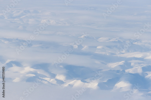 Aerial view of snow-capped mountains and clouds. Winter snowy mountain landscape. Icheghem Range, Kolyma Mountains. Koryak Okrug (Koryakia), Kamchatka Krai, Siberia, Far East Russia. Great background.
