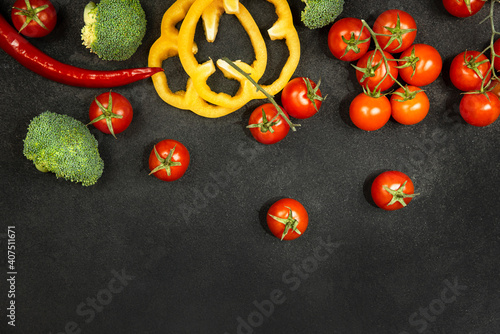 Vegetables, sweet yellow peppers, chili peppers, broccoli, cherry tomatoes on a black background.