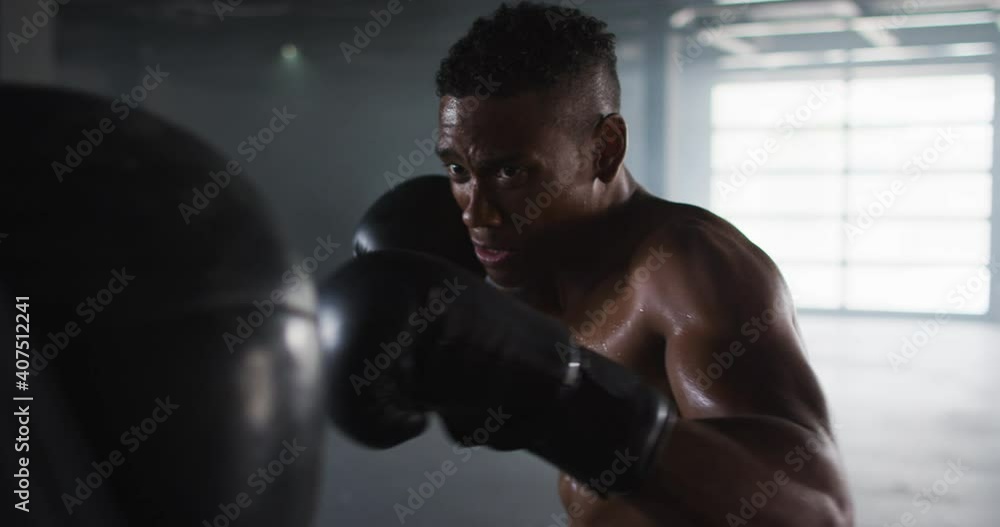 African american man wearing boxing gloves training in empty building punching punchbag African american man wearing boxing gloves training in empty building punching punchbag
