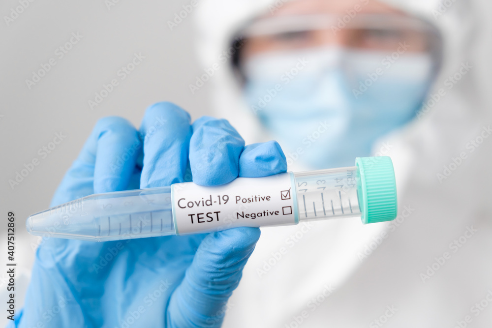 Doctor wearing disposable coverall or protective PPE suit with mask and safety google holding a test tube with positive Covid-19 test result. Doctor wearing disposable coverall or protective PPE suit with mask and safety google holding a test tube with positive Covid-19 test result.