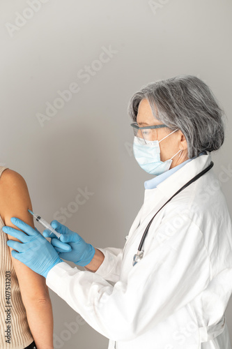 Side view portrait of a senior female doctor healthcare professional wearing protective mask and sterile gloves  holding a syringe  injecting flu or coronavirus vaccine for the immunity and prevention