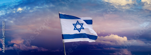 Israeli flag with a star of David over Jerusalem at cloudy sky background on sunset, panoramic view.