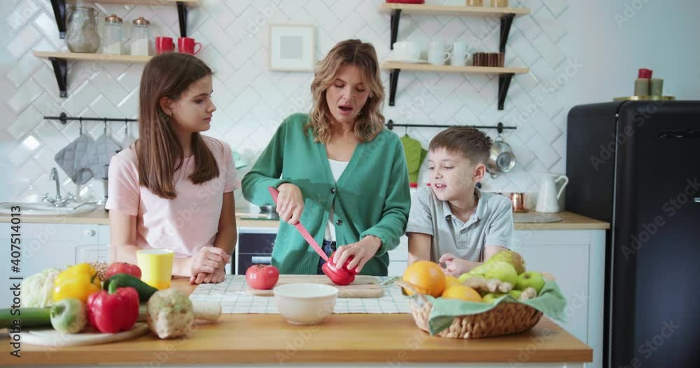 Young family in the kitchen preparing lunch together cutting fresh vegetables on wooden desk. Cozy home. Children with mother. Upbringing. Young family in the kitchen preparing lunch together cutting fresh vegetables on wooden desk. Cozy home. Children with mother. Upbringing.