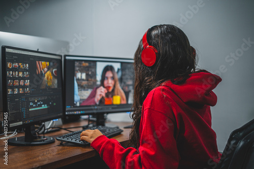 Mujer joven editando video en dos monitores con audífonos sudadera roja