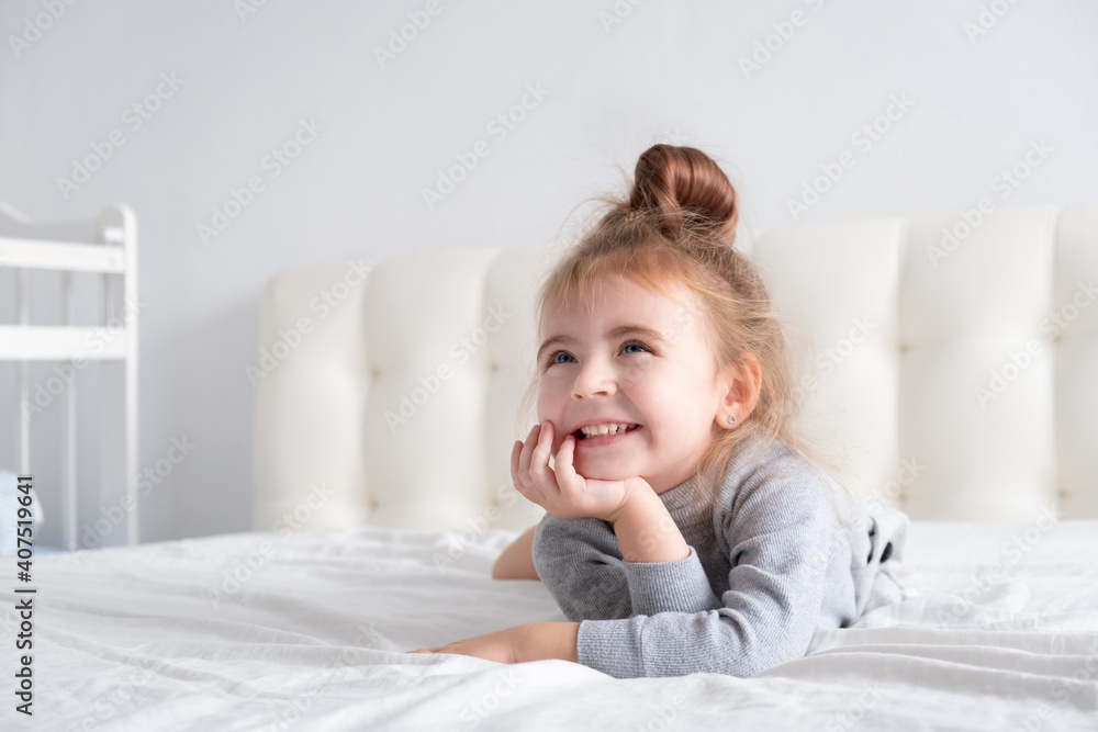 little girl in grey turtleneck having fun on white bedding little girl in grey turtleneck having fun on white bedding