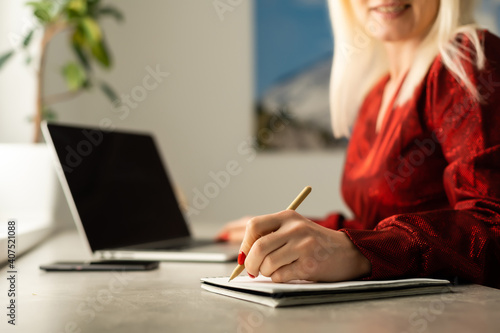 Young woman with laptop writes in notepad