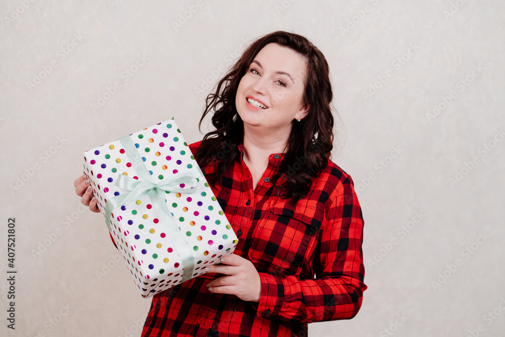 Attractive woman in a red checkered dress with a gift against the white wall. Attractive woman in a red checkered dress with a gift against the white wall.